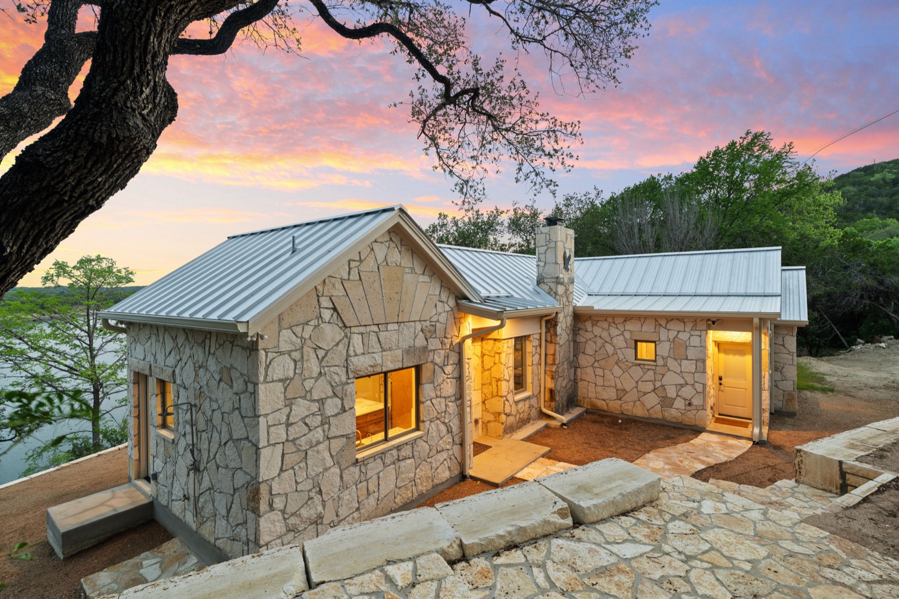 Stone custom home surrounded by mature trees at twilight